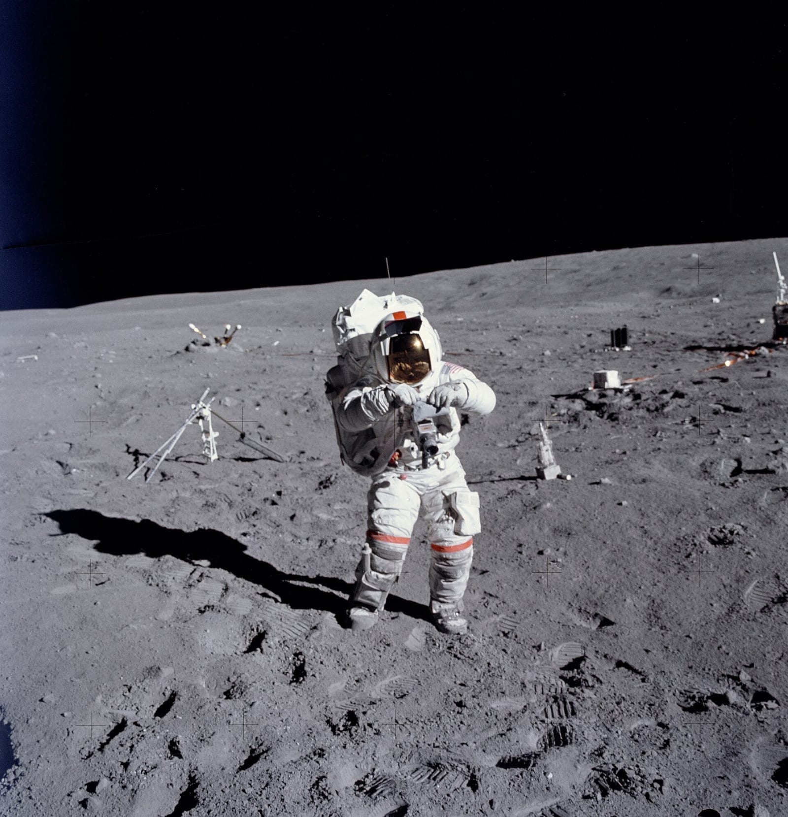 An Apollo astronaut standing on the lunar surface beside scientific equipment