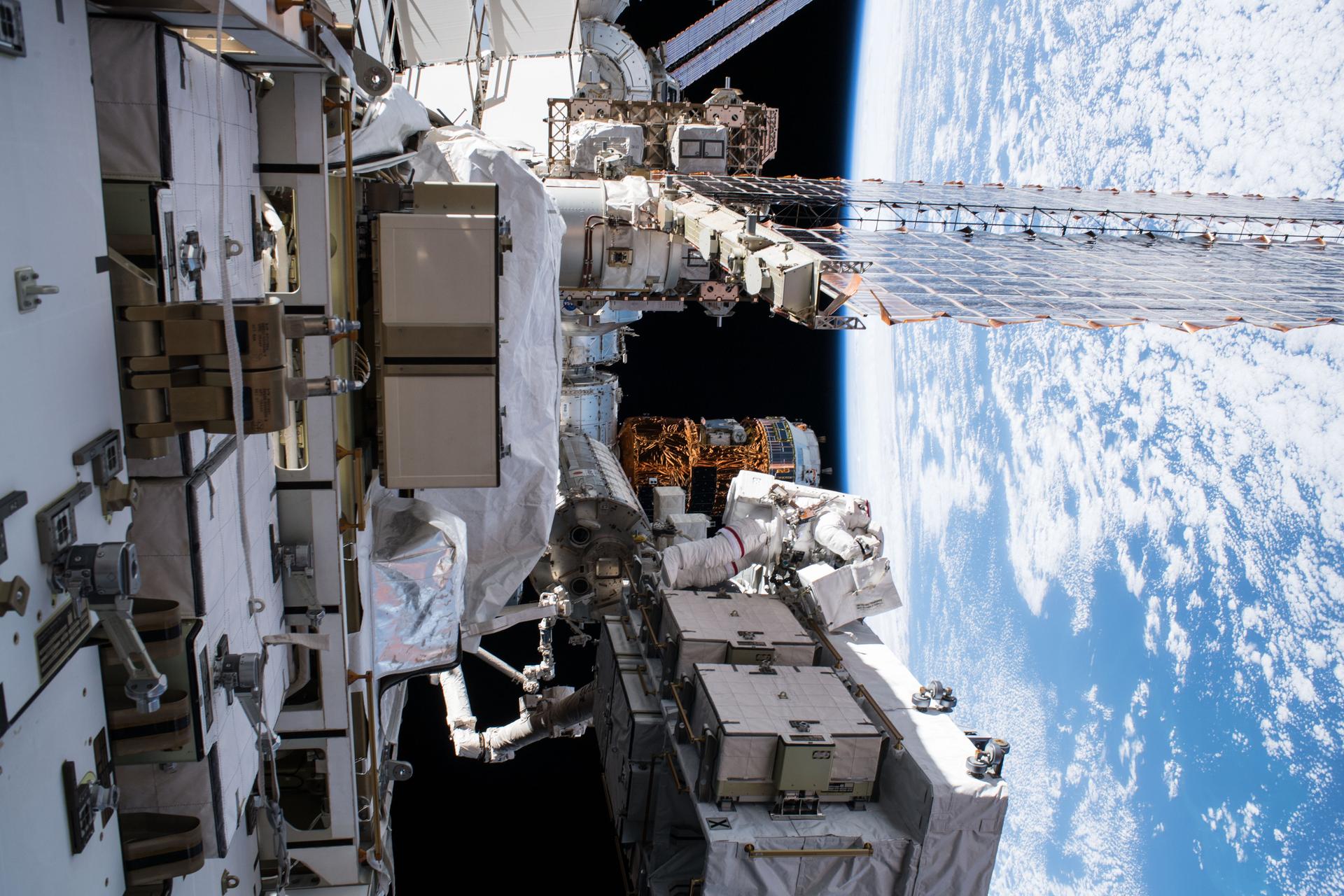 An astronaut in a white spacesuit on a spacewalk outside the International Space Station, with Earth below